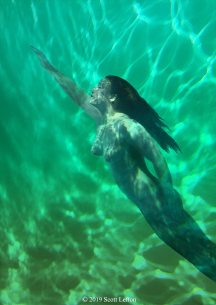 A woman swims upwards through deep water.