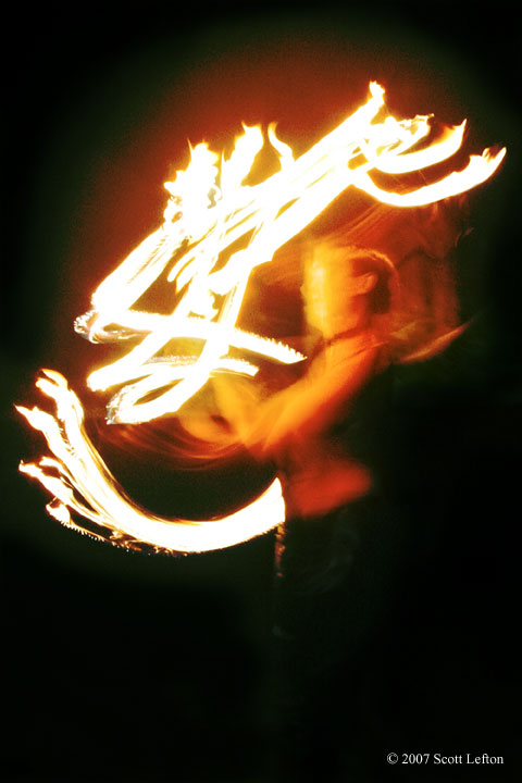 She Writes With Calligraphy Of Fire - A woman dancing with fire fans creates shapes in the air that look like calligraphy.