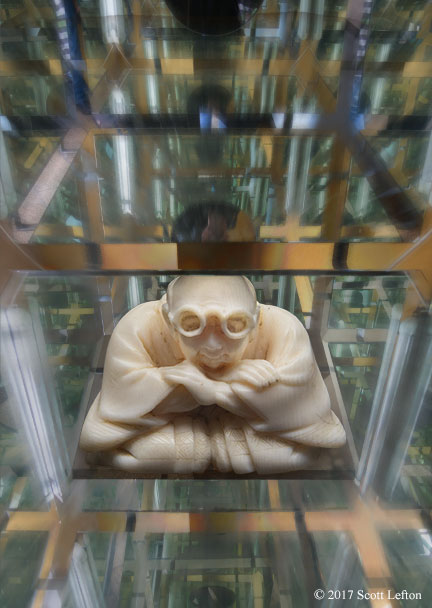 A carved ivory figure sits crosslegged, serene and bespectacled amidst an apparently infinite grid extending in all directions.