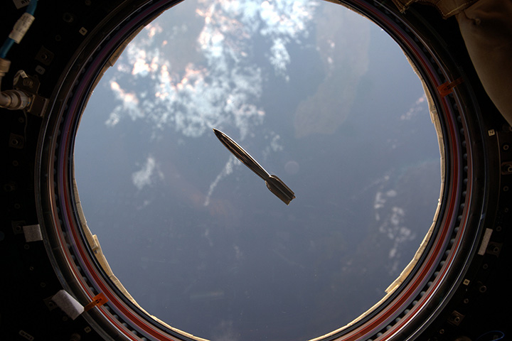 The Mini Hugo Rocket floats in the International Space Station in front of a window overlooking the Earth.
