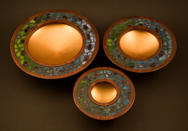Top view of three mosaic bowls in dark reddish mahogany with green, blue and purple stained glass mosaic inlay, looking somewhat Tiffany.  The inside surfaces are finished in gold acrylic paiint.