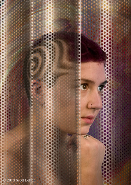 A woman with spiral designs in her hair peers out from behind a steel mesh